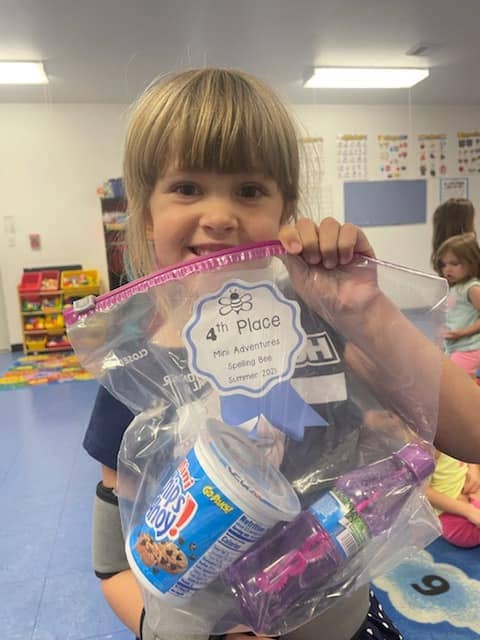 Child at Mini Adventures Preschool in Warrensburg, MO holding a 4th place award from a spelling bee.