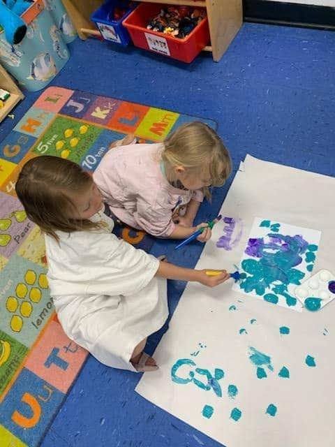 Children painting on the floor during a creative session at Mini Adventures Preschool & Daycare in Warrensburg, MO.