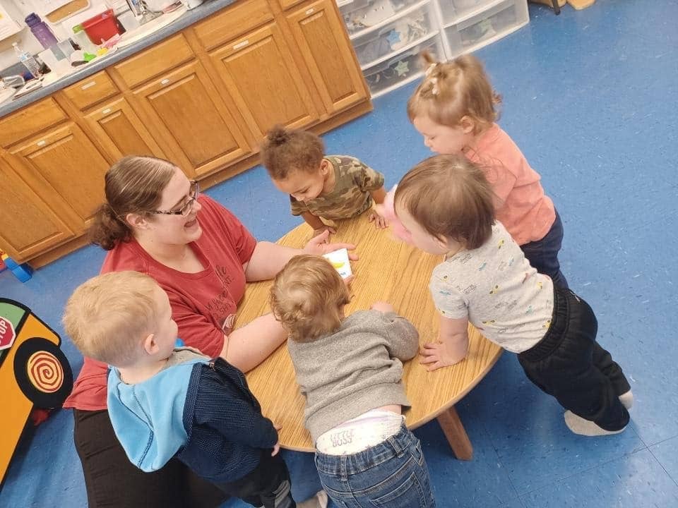 Toddlers engage in play-based learning with teacher at Warrensburg daycare.